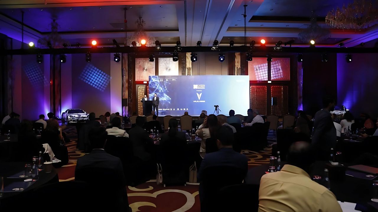 A ballroom set with round tables faces a lit stage as a forum session begins.