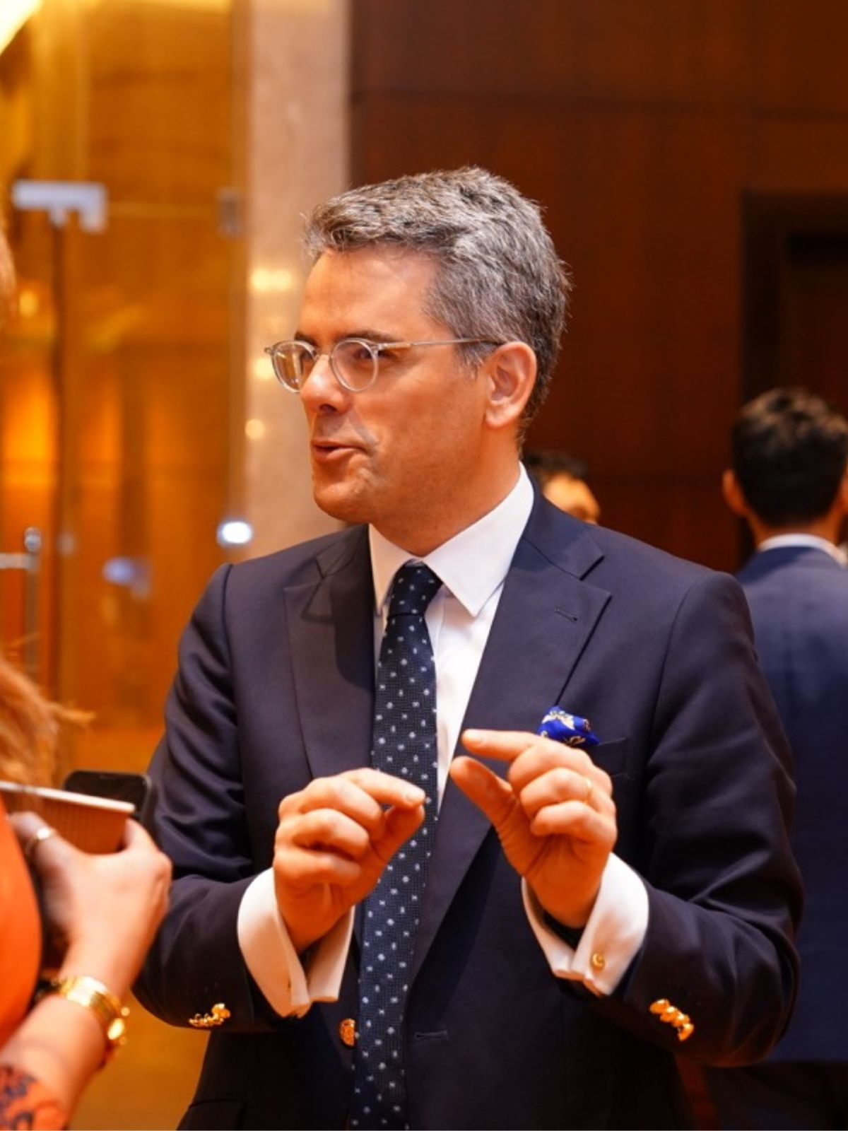 An executive in a navy suit gestures as he makes a point in conversation.